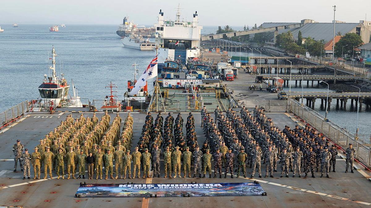 A large group of military personnel stand in formation on the landing deck of a ship.