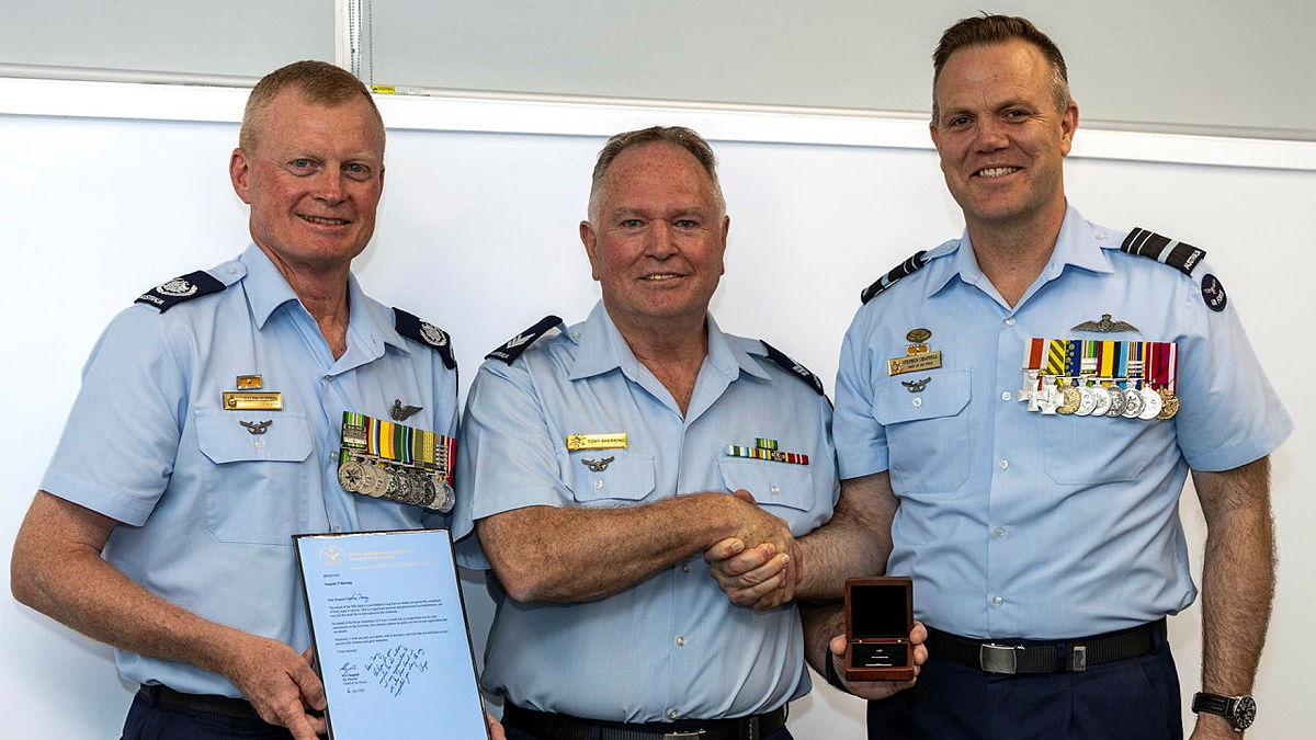 Three men in Air Force uniforms stand together with two of them shaking hands.