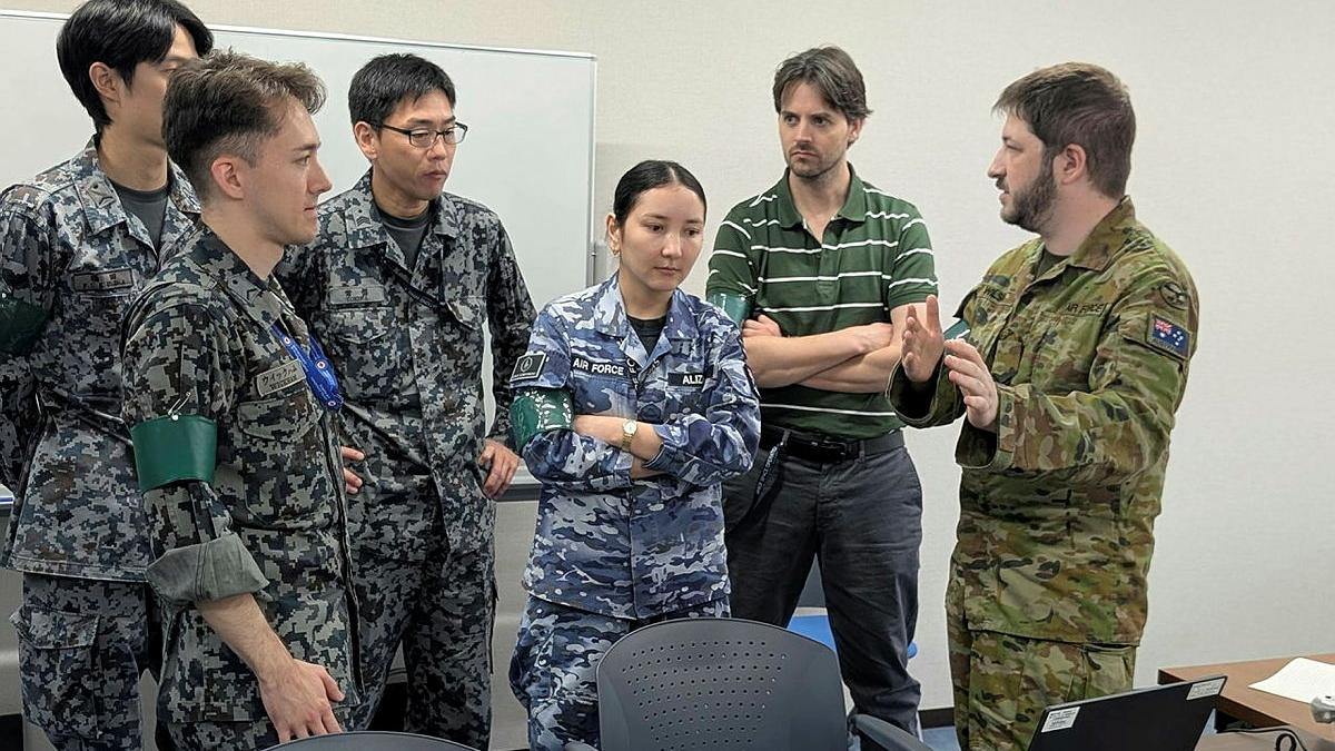 A group of military members and a civilian engage in discussion in an office area.