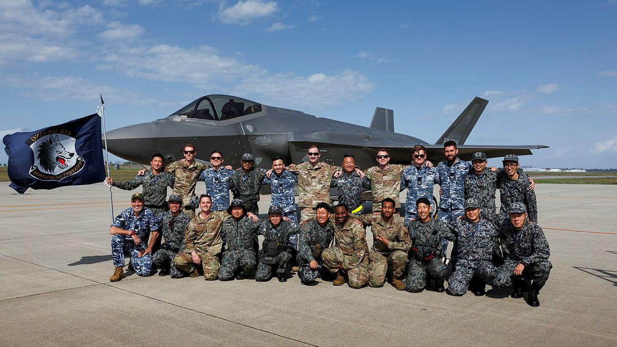 A group of military personnel with a flag and an aircraft behind them while on the tarmac.