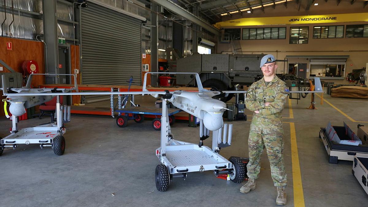 A man in uniform stands next to a small aircraft in a warehouse.