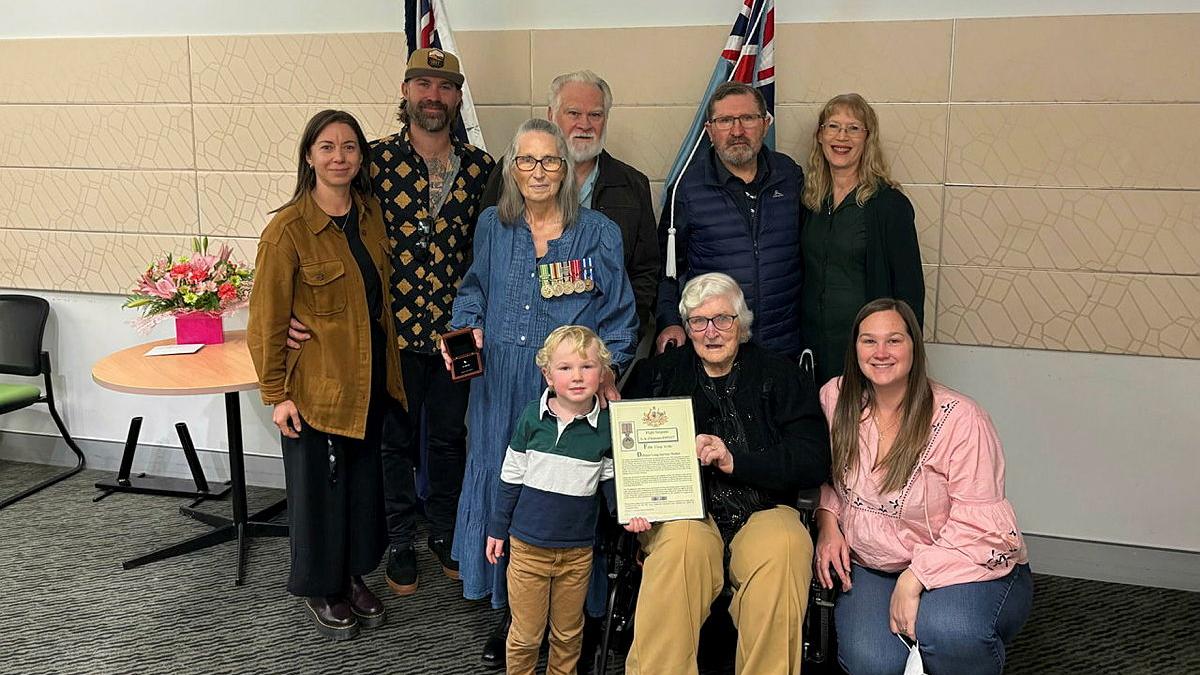 A woman with military medals stands with her family and a paper award.